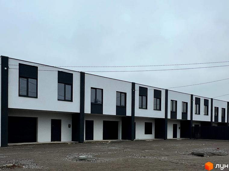 Зовнішній вигляд новобудови на вул. Дружби з білими фасадами та темними вікнами. Перед будинком розташована прибудинкова територія з гравієм та парканом.