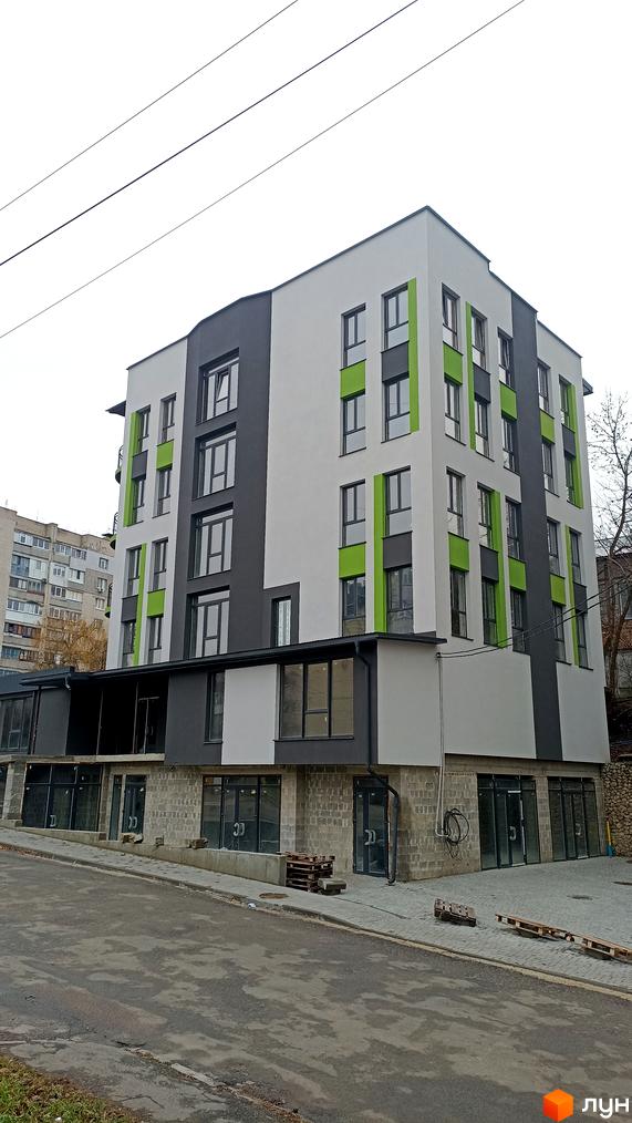 Зовнішній вигляд новобудови на вул. Наливайка, 1, з сірими та зеленими акцентами та великими вікнами. На прибудинковій території видно дорогу та тротуар.