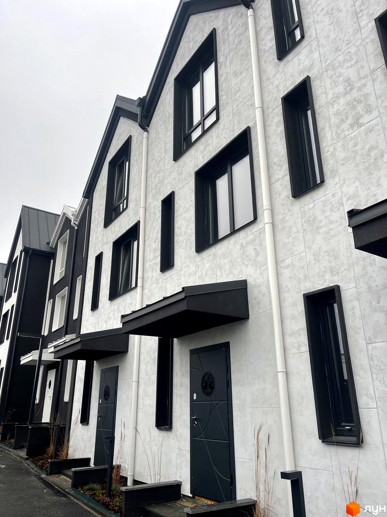 Зовнішній вигляд таунхаусів New Smart 15 з білою та чорною обробкою, великими вікнами та вхідними групами. Навколо будинків облаштована прибудинкова територія з рослинністю.