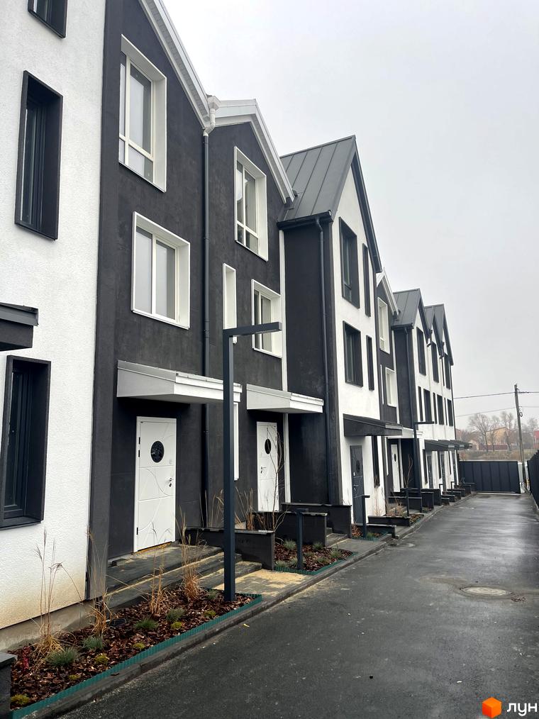 Таунхаус New Smart 15 з чорно-білими фасадами та сірим дахом. Прибудинкова територія з доглянутими клумбами та асфальтованою доріжкою.