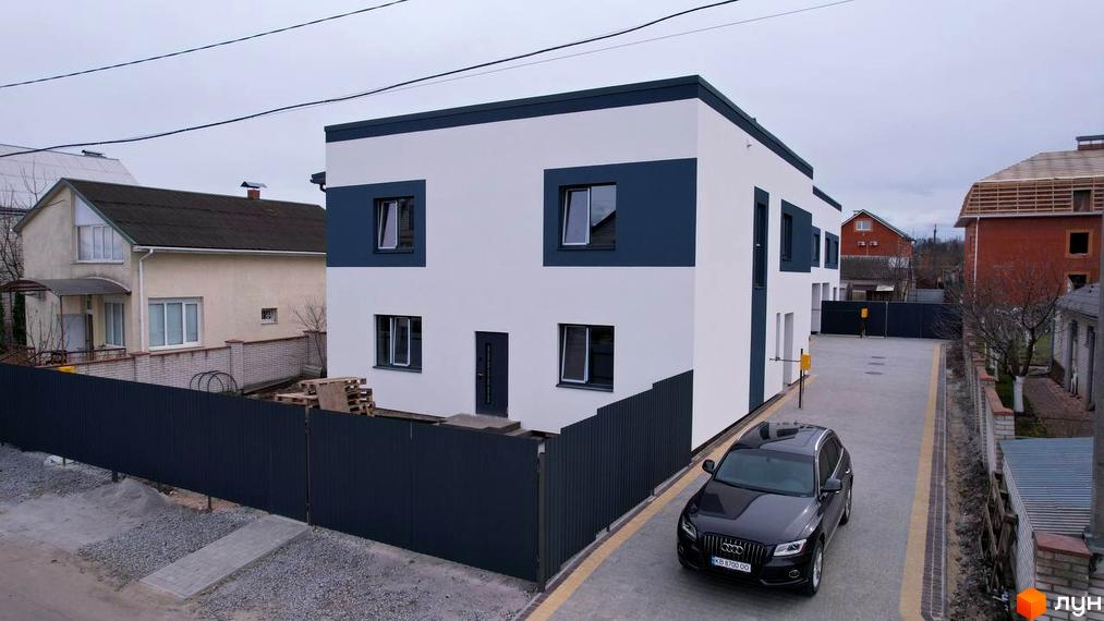 Новобудова Дуплекси Флагман Хутори з біло-синім фасадом та прибудинковою територією, де припаркований чорний автомобіль.