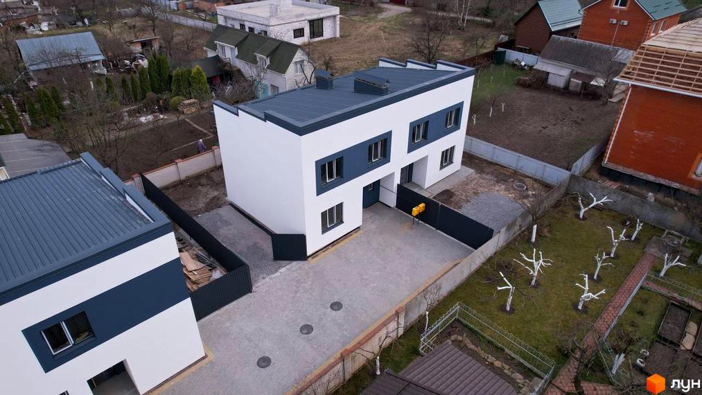 Білий двоповерховий будинок з темно-синіми вставками та сірим дахом. На подвір'ї бруківка, газон з деревами.