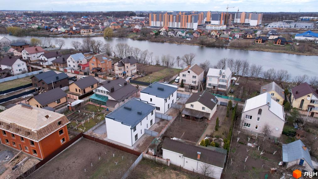 Білі двоповерхові будинки з темно-сірими дахами в житловому районі. Навколо будинку є прибудинкова територія з газоном та огорожею.