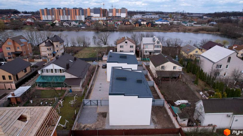 Сучасні дуплекси Флагман Хутори з сірими дахами та білими фасадами, розташовані біля водойми та зеленої зони. На території комплексу є доглянуті дворики та сусідні будинки.