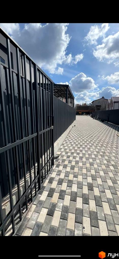 Огорожа та бруківка біля житлового комплексу. Дорога з бруківки веде до будинків з темним парканом.