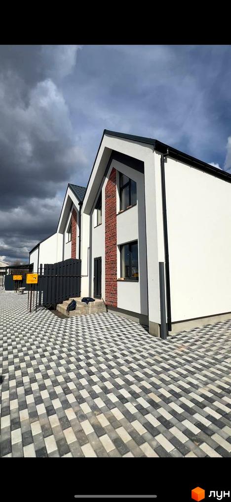 Дуплекси Флагман Стрижавка: фасади будинків з цегляними вставками та сіра огорожа на тлі хмарного неба. Територія перед будинками викладена плиткою сіро-білого кольору.