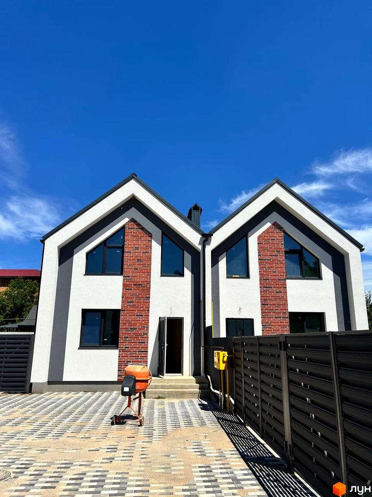 Двоповерховий будинок з білими стінами та цегляним фасадом. На подвір'ї бруківка та чорний паркан.