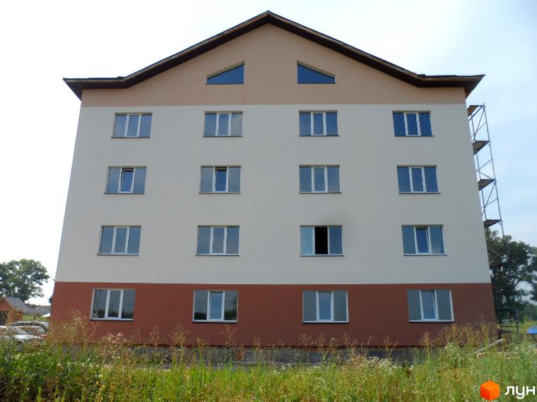 Зображення фасаду чотириповерхового будинку в Житловому комплексі Фізкультурний. Навколо будинку зелена трава.