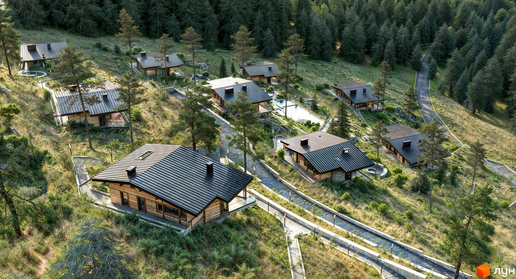 Котеджне містечко КМ Veres Hill: дерев'яні будинки з темними дахами, розташовані на схилі гори серед хвойного лісу. На території є басейн та доріжки.