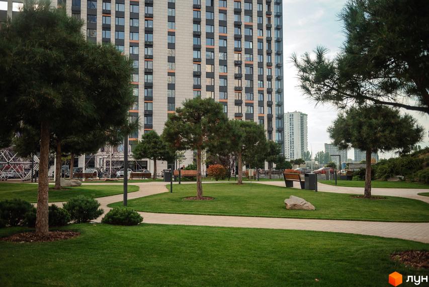 Житловий комплекс Метрополіс. Фасад багатоповерхового будинку з великою кількістю вікон. Прибудинкова територія з зеленим газоном, деревами та доріжками.