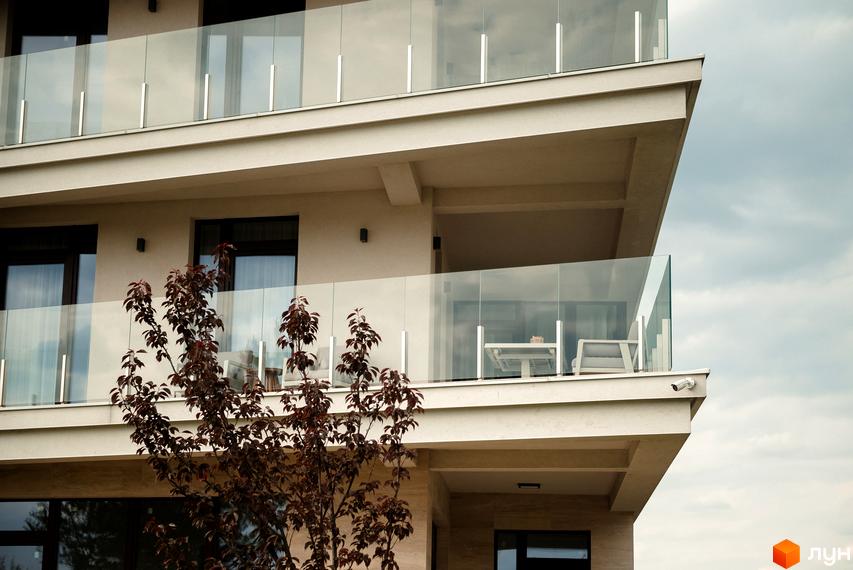 Зовнішній вигляд житлового комплексу Park Lake City з балконами та скляними перилами. На одному з балконів видно столики та крісла.