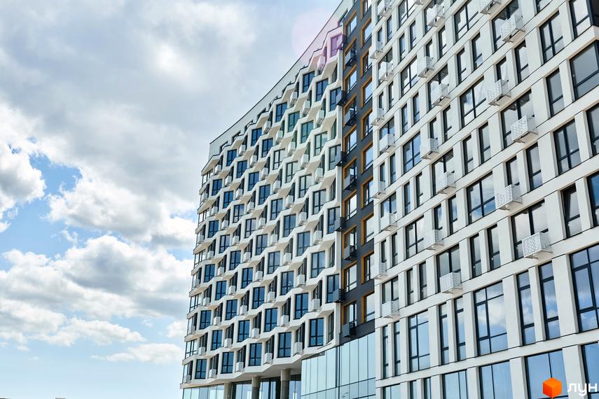 Житловий комплекс LUCKY LAND з білим фасадом, вікнами геометричної форми та декоративними елементами. На першому поверсі великі скляні вітрини.