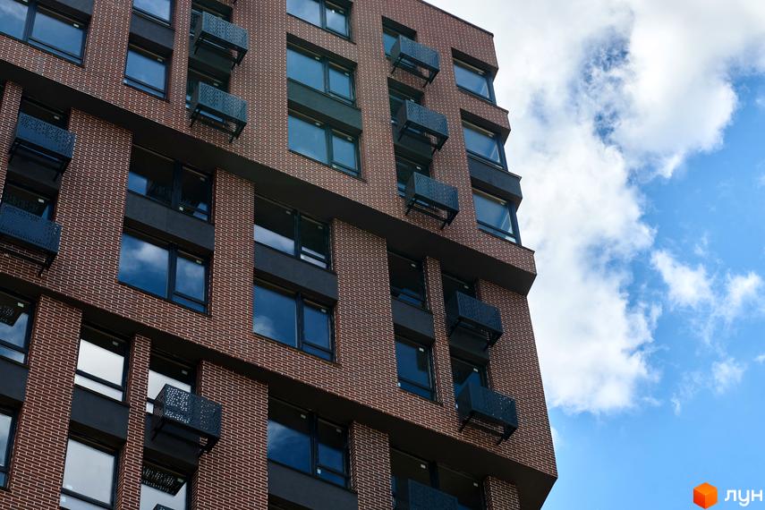 Багатоповерховий цегляний будинок Житлового комплексу LUCKY LAND з темними вікнами та металевими конструкціями на фасаді під блакитним небом.