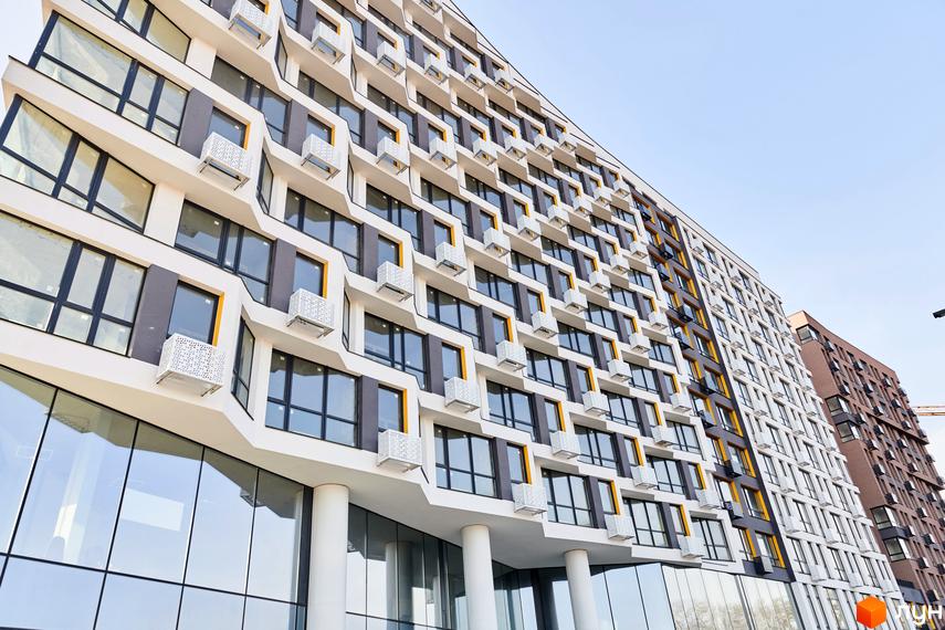 Житловий комплекс LUCKY LAND: багатоповерховий будинок з хвилястим фасадом білого та темно-сірого кольорів, вікнами з жовтими рамами та білими коробами для кондиціонерів.