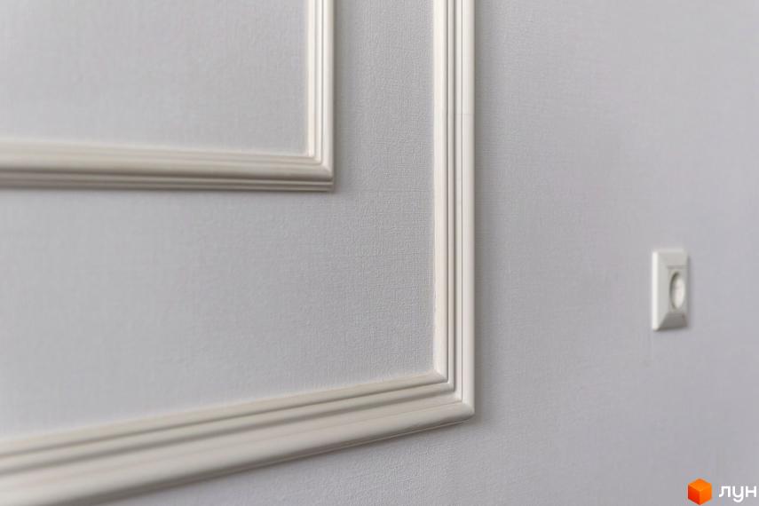 Деталі інтер'єру Житлового комплексу „Кагарлицький“: світла стіна з текстурою, оздоблена декоративними молдингами та електричною розеткою.