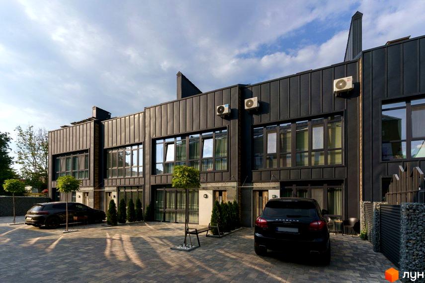Таунхаус Black edition - це комплекс із сучасними фасадами чорного кольору та великими вікнами, розташований на вимощеній бруківкою території з зеленими насадженнями та автомобілями.