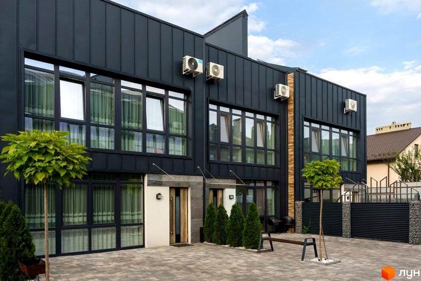 Таунхаус Black edition – двоповерховий будинок з великими вікнами та чорним фасадом, розташований на вимощеній плиткою території з деревами та лавкою.
