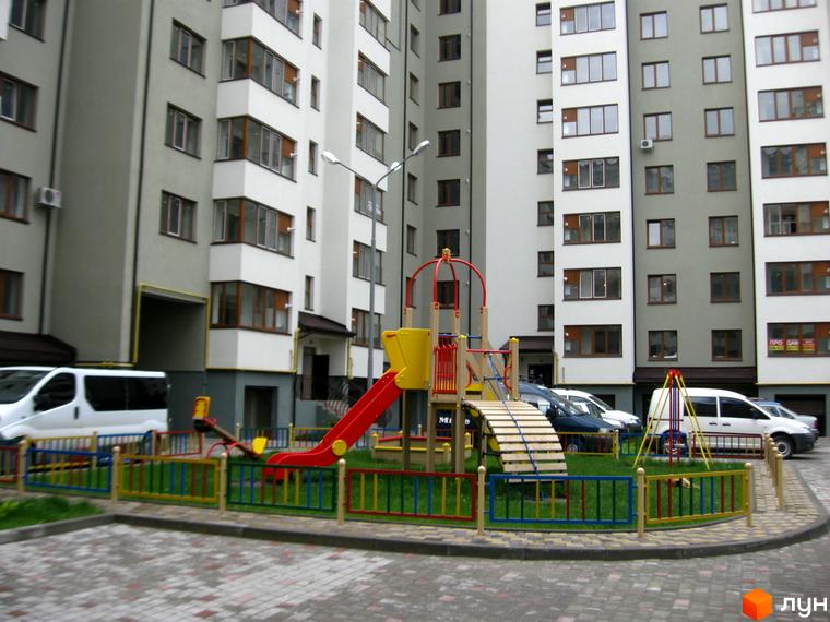 Зображення житлового комплексу на вулиці Хотинській. На фото дитячий майданчик з гіркою та гойдалкою, а також багатоквартирний будинок.