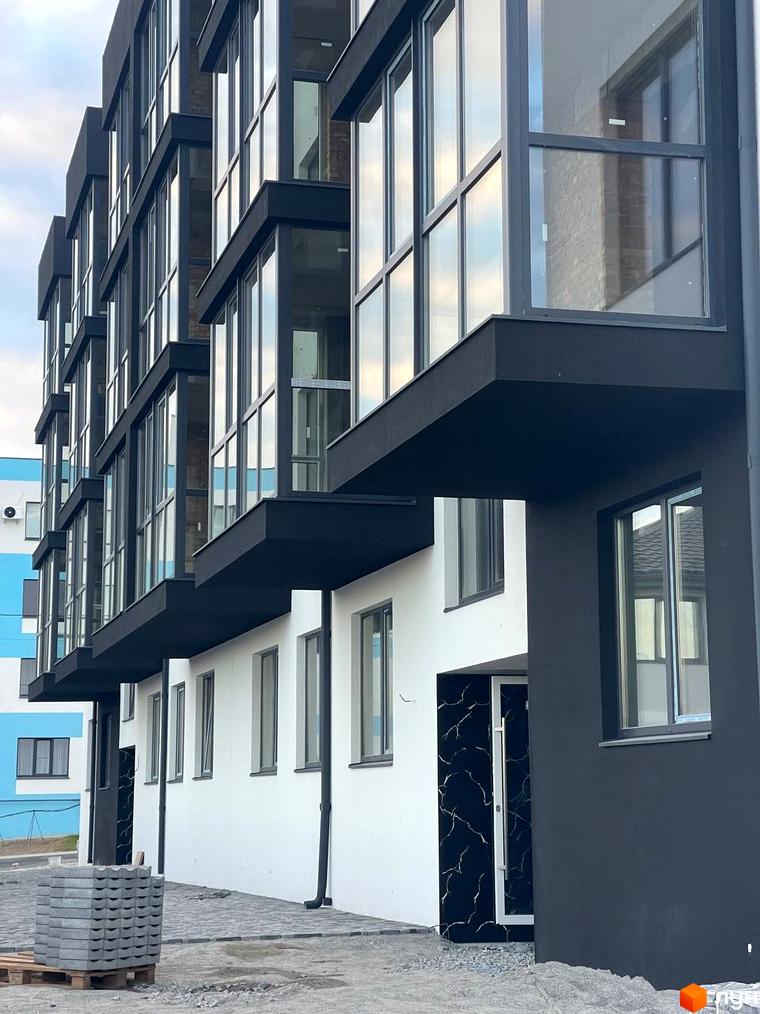 Фасад Житлового комплексу на вул. Фабрична з чорно-білим оздобленням та скляними балконами. Прибудинкова територія вимощена бруківкою.