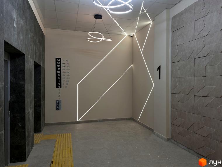 Сучасний дизайн холу житлового комплексу ЖК SOURENGE з підсвіткою та оздобленням стін. Поруч розташовані ліфти та вказівники поверхів.