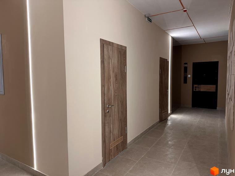 Коридор у житловому комплексі ЖК SOURENGE з дерев'яними дверима та підсвіткою стін. Оздоблення підлоги плиткою.