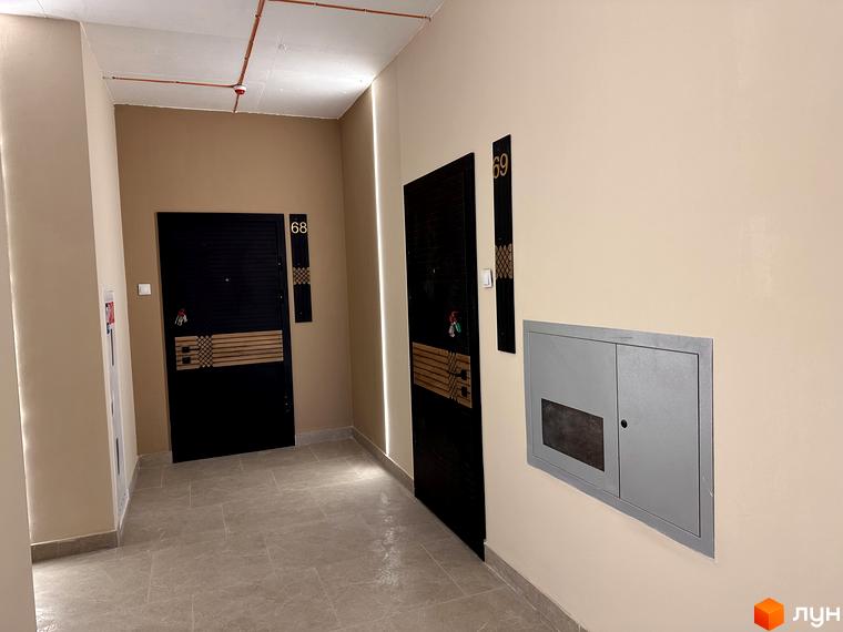 Коридор з дверима під номерами 68 та 69 у новобудові ЖК СОУРЕНЖ. Сіра шафа на стіні та труби на стелі.