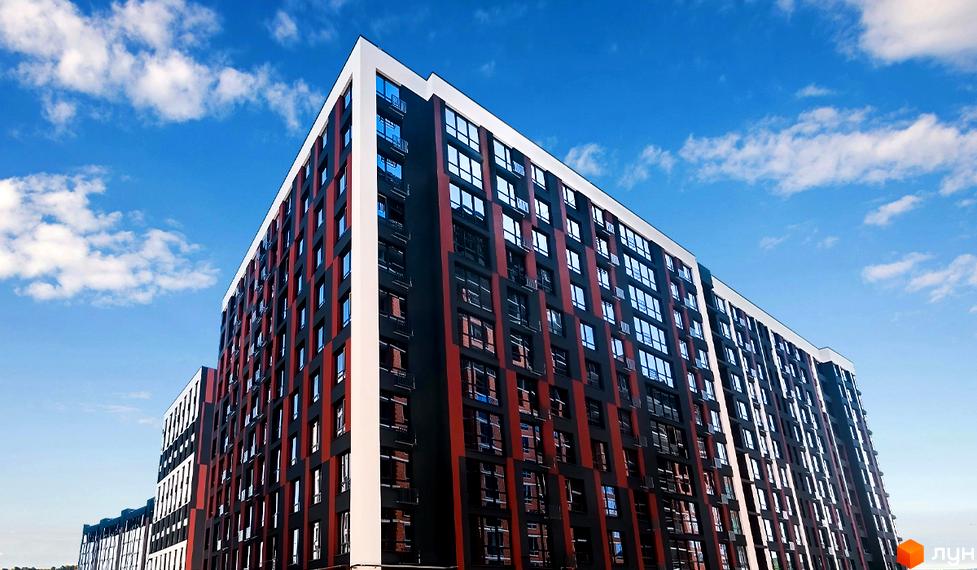 Зображення фасаду багатоповерхового будинку в Житловому комплексі Паркова Алея. Вигляд новобудови з великою кількістю вікон на фоні блакитного неба.