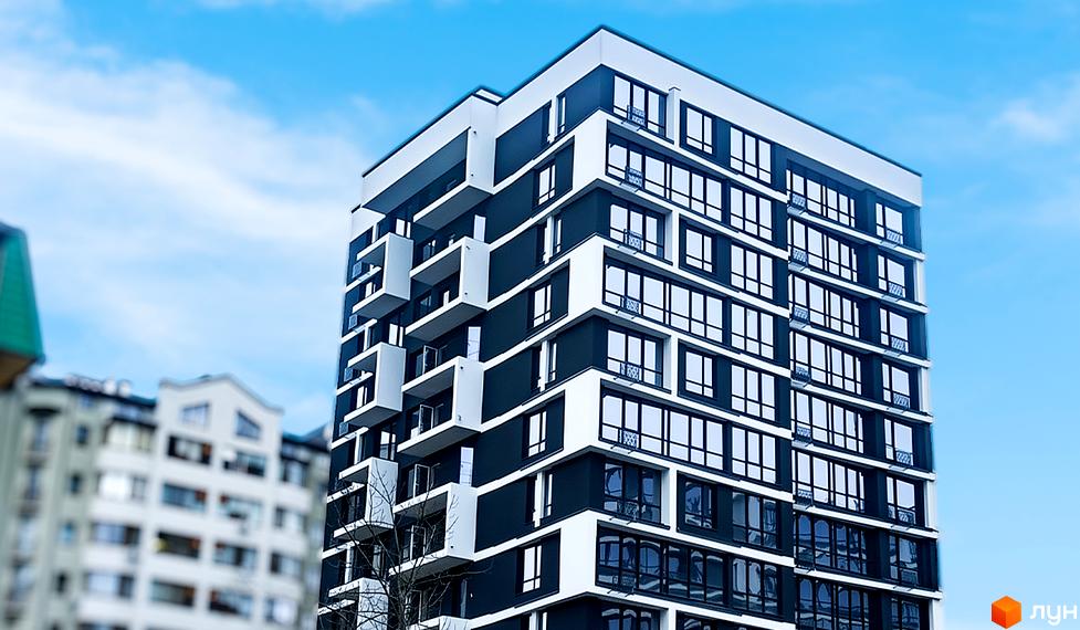 Фасад житлового комплексу А5 з панорамними вікнами та балконами. Навколо видно інші будинки та блакитне небо.