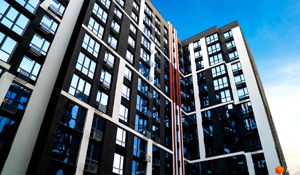 Багатоповерховий будинок ЖК U One з великими вікнами та балконами на тлі блакитного неба. Фасад будівлі виконаний в чорно-білих кольорах.