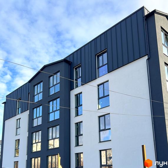 Зовнішній вигляд новобудови на вул. Різдвяна, 108, з біло-сірими фасадами та великими вікнами. Будівельний проєкт з металевим дахом.