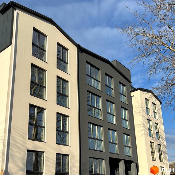 Фасад житлового комплексу на Різдвяній, 108, з вікнами та сірими та бежевими елементами. Навколо видно гілки дерев та блакитне небо.