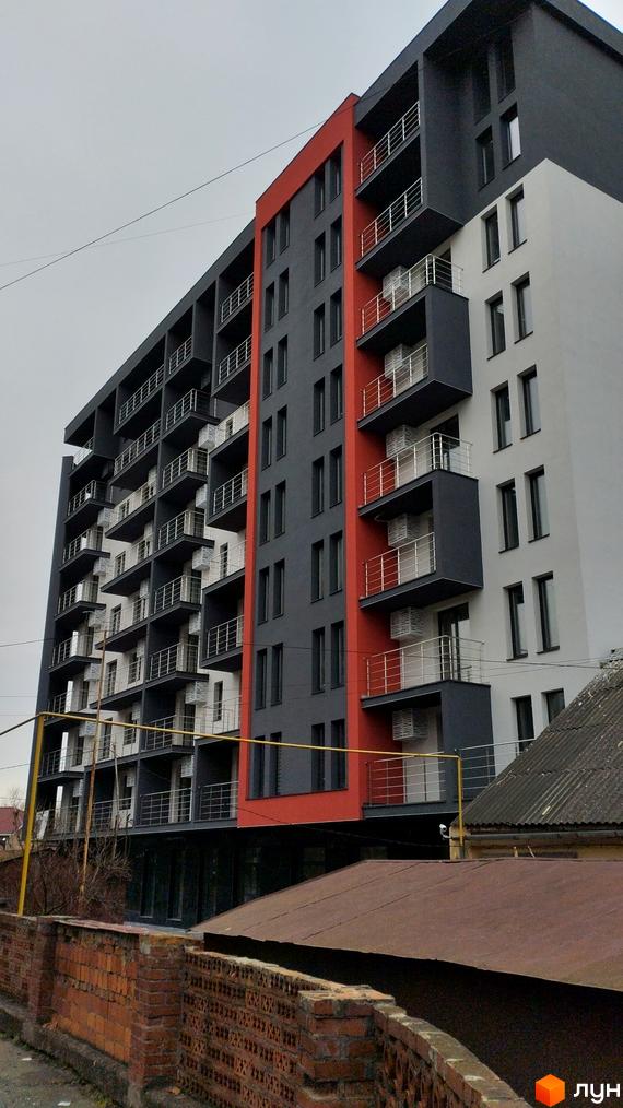 Багатоповерховий будинок ЖК City Park з балконами та фасадом у сірих і червоних тонах. На передньому плані цегляний паркан.