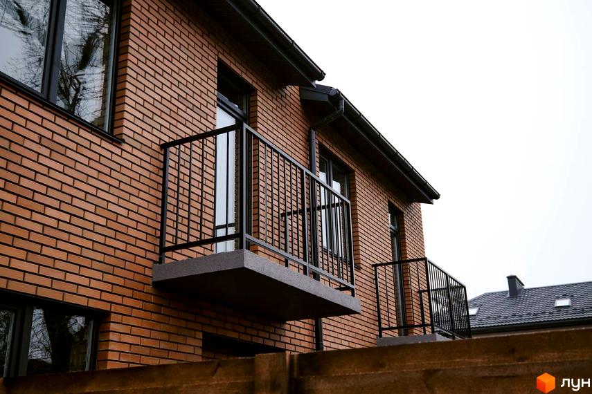 Фасад будинку з червоної цегли з балконами та вікнами в житловому комплексі Позітано Центр 2. Видно сусідній дах.