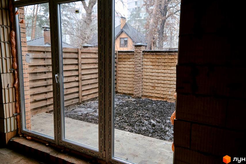 Таунхауси Позітано Центр 2: вид з вікна на двір з дерев'яним парканом та цегляною стіною. Будівельний проєкт з прибудинковою територією.