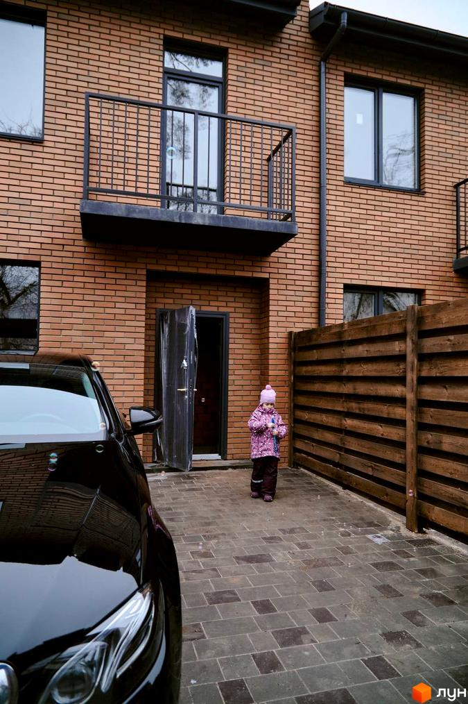 Таунхауси „Позітано Центр 2“: цегляний будинок з балконом та вікнами, поруч дитина та авто на вимощеній території.