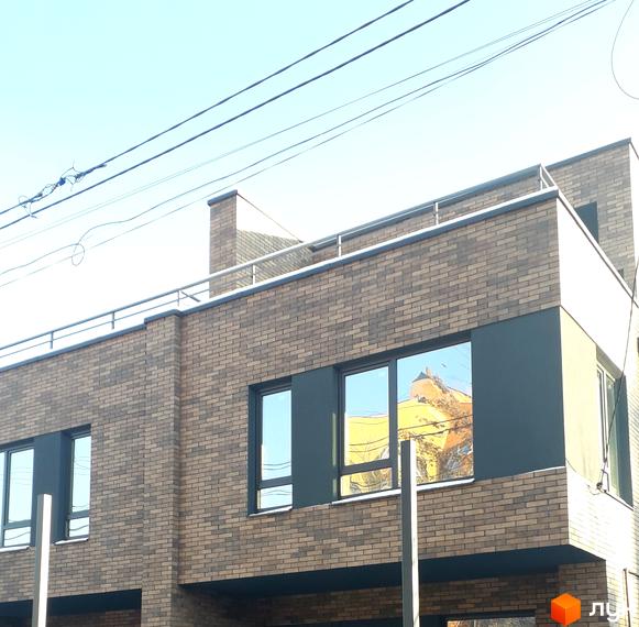 Фасад житлового комплексу на вулиці Новий Світ-бічна, 13, з цегляним оздобленням та великими вікнами. Навколо будинку видно елементи інфраструктури та чисте небо.