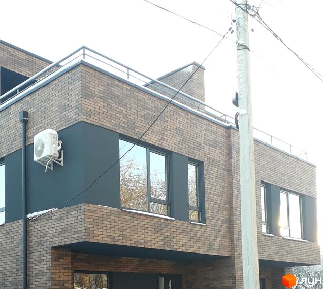 Фасад новобудови на вул. Новий Світ-бічна, 13, з цегляним оздобленням та великими вікнами. Поруч розташована електроопора.