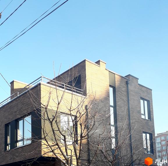 Фасад новобудови на вулиці Новий Світ-бічна, 13, оздоблений цеглою. Навколо будівлі видно голі дерева та синє небо.