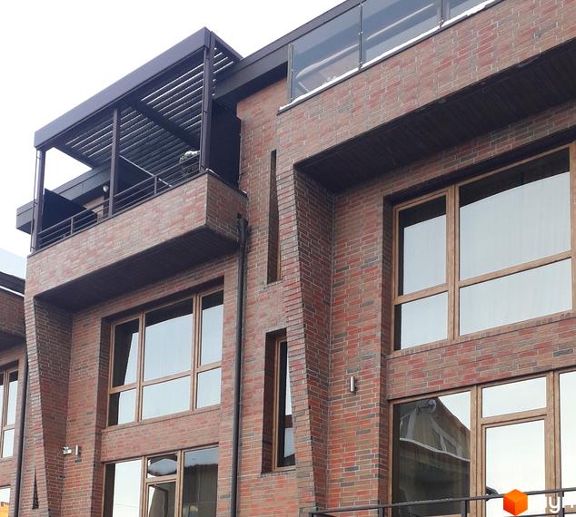 Фасад будинку з червоної цегли з великими вікнами та балконом на вулиці Вільхова, 7в. Зовнішній вигляд новобудови з елементами сучасної архітектури.