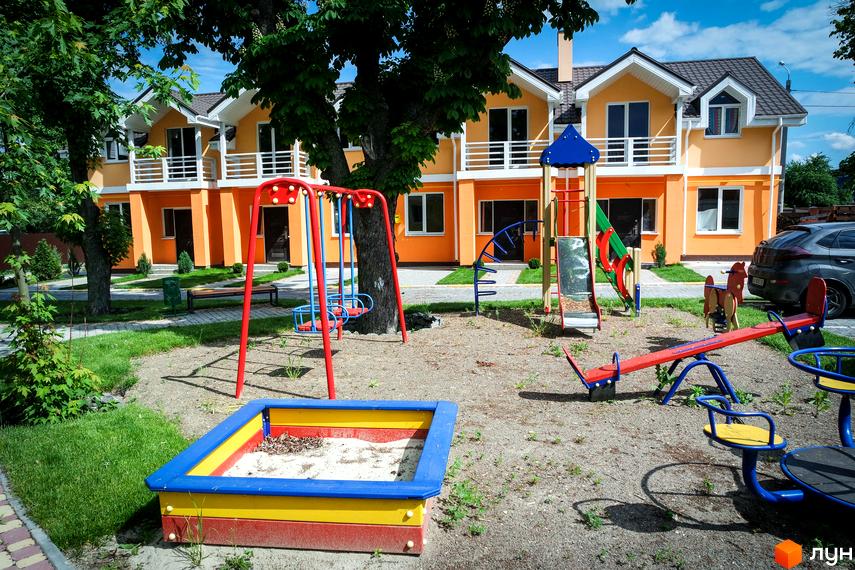 Зображення Котеджного містечка Sun City з дитячим майданчиком. Двоповерхові будинки з помаранчевими фасадами та білими балконами.