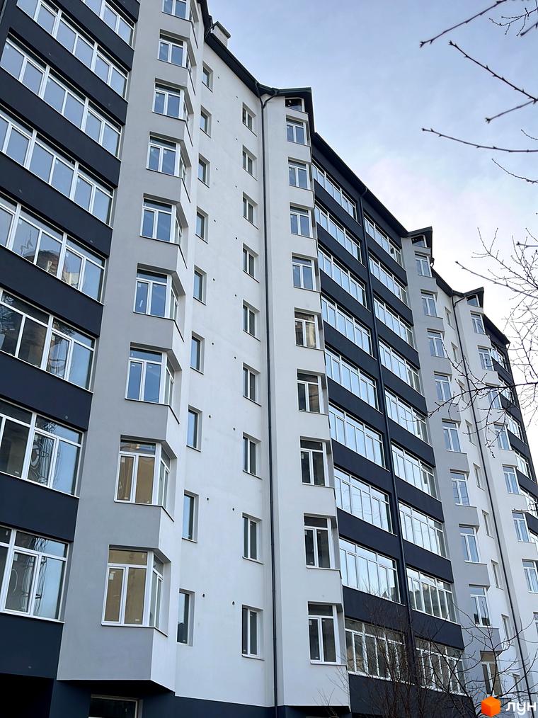 Фасад житлового комплексу на вул. Лемківська, 3 з сірими та темно-сірими секціями, численними вікнами та еркерами. Видно голі гілки дерев.