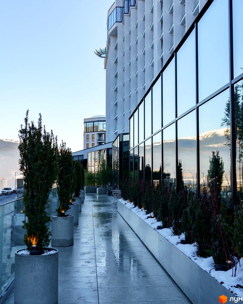 Апарт-комплекс Mountain Residence з панорамним склінням та озелененою терасою. Зовнішній вигляд будівлі, тераса з деревами в діжках та гірський пейзаж.