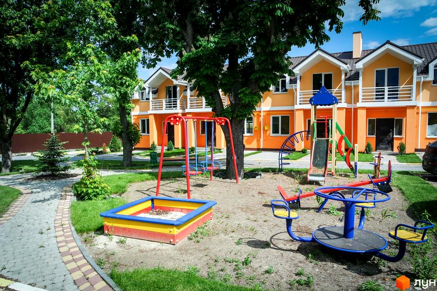 Фото Котеджного містечка Sun City з дитячим майданчиком. Двоповерхові котеджі помаранчевого кольору з білими балконами, зелена територія.