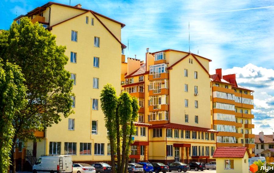 Зовнішній вигляд Житлового району Чабани квартал: кілька жовтих будинків різної поверховості з червоними дахами. На передньому плані дерева та припарковані автомобілі.