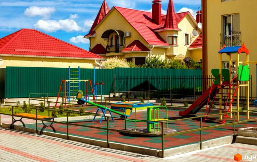 Зображення дитячого майданчика біля будинків у Житловому комплексі Чабани квартал. На фото будівлі з червоними дахами та зелений паркан.
