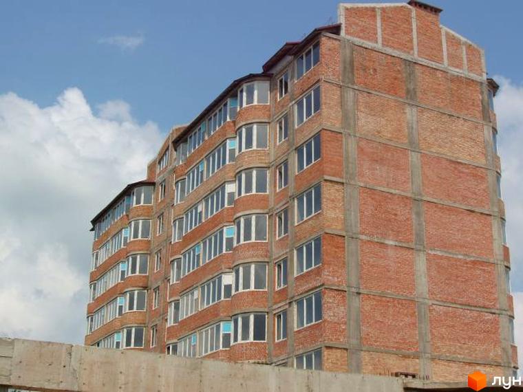 Фото недобудованого будинку в Житловому комплексі Зелений берег. Цегляна багатоповерхівка з великими вікнами на фоні блакитного неба.