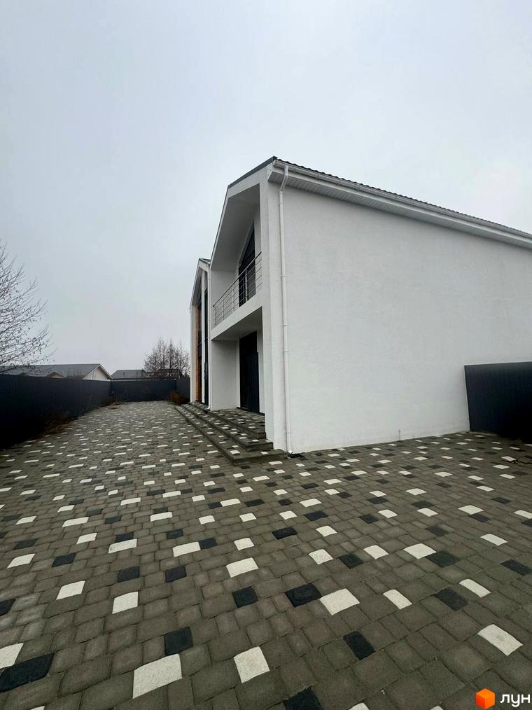 Білий дуплекс Family House з темним дахом та балконом. Перед будинком вимощена територія з візерунком з плитки.