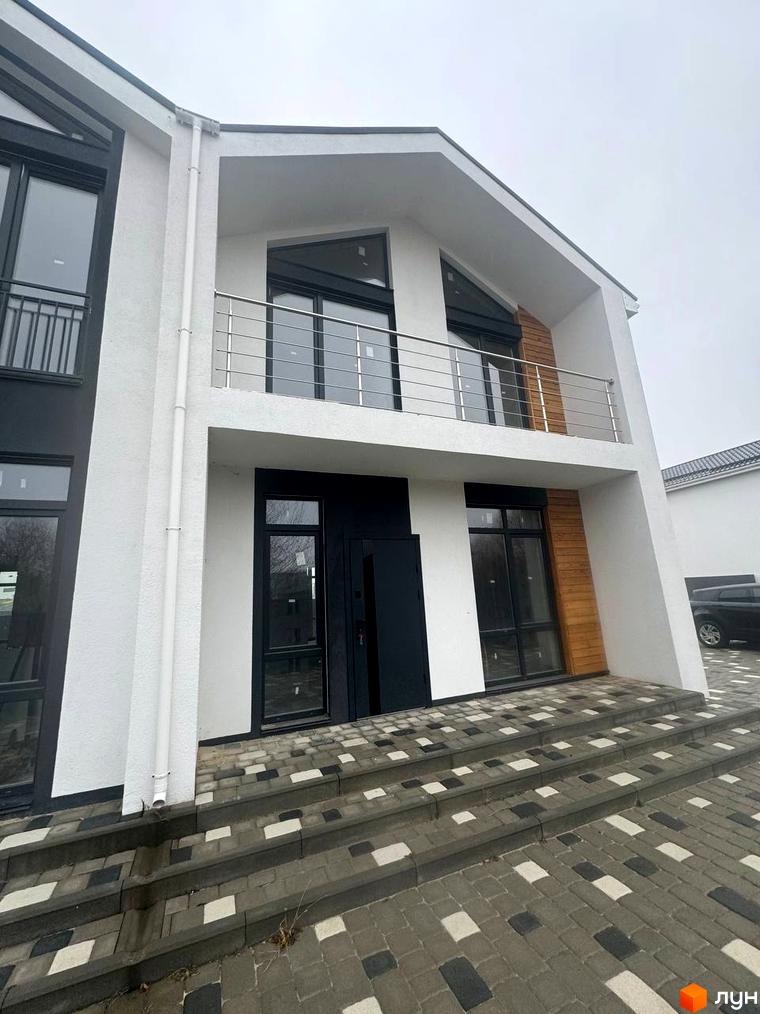 Фасад дуплексу Family House білого кольору з чорними вікнами та дерев'яними елементами. Перед будинком укладена бруківка сірих відтінків.