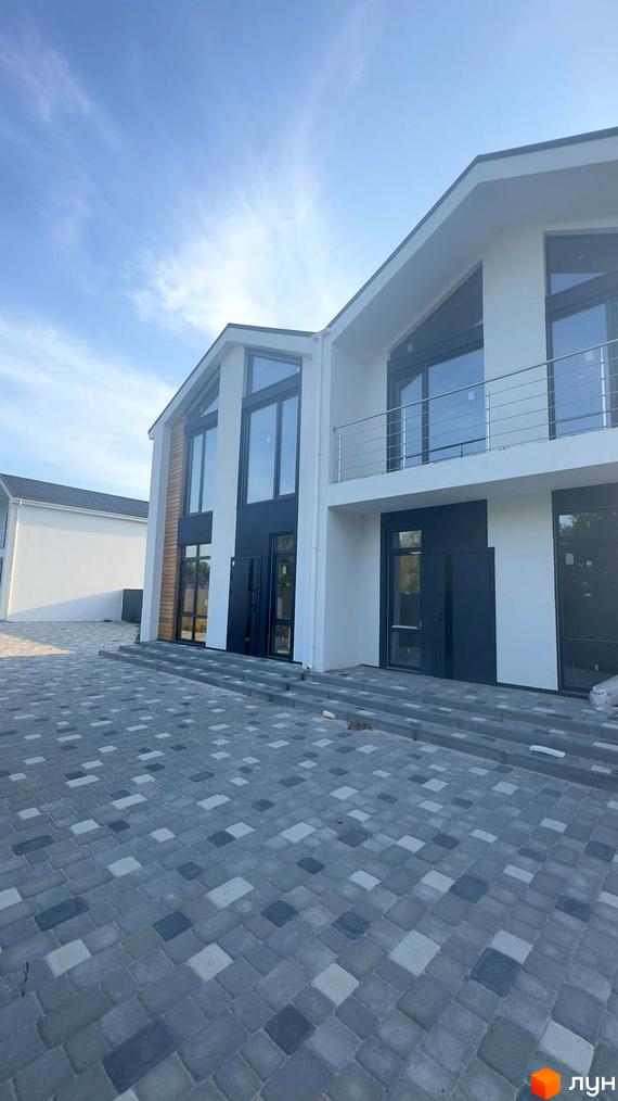 Зовнішній вигляд дуплексів Family House з великими вікнами та сірим бруківкою перед будинком. Сучасна забудова з елегантною архітектурою.