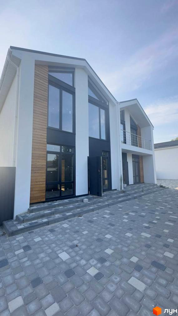 Фасад дуплексу Family House: білі стіни, великі темні вікна, дерев'яні панелі. Перед будинком укладена сіра бруківка.